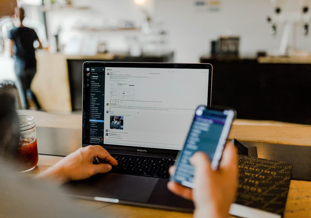 A person using a laptop and phone at a table